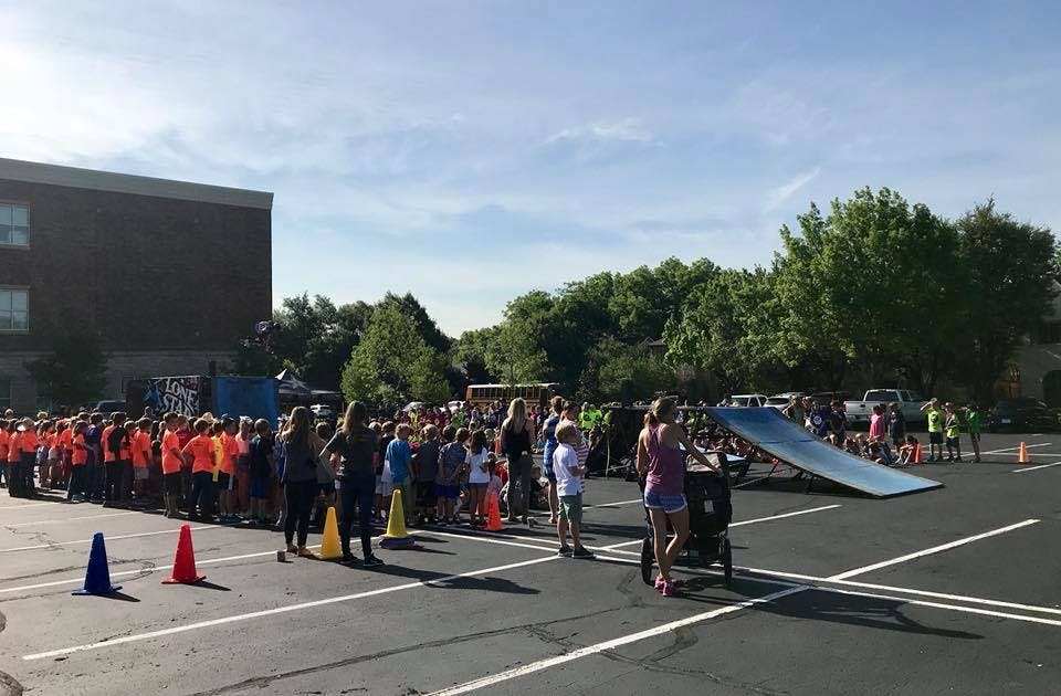 People gathered in a parking lot with a long line of children in orange shirts