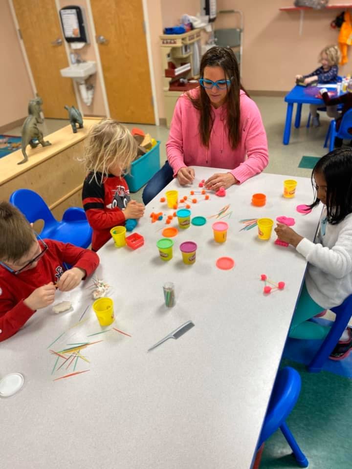 Adult and children playing with colorful playdough at a table
