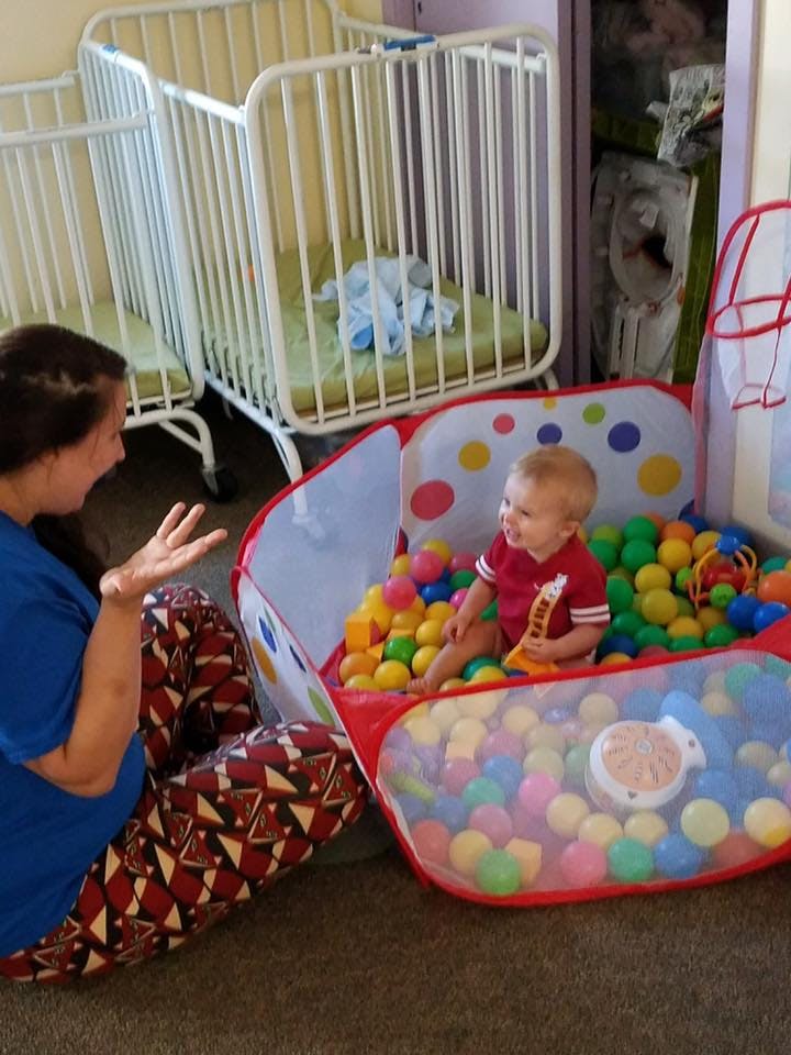 Person sitting next to a child in a ball pit