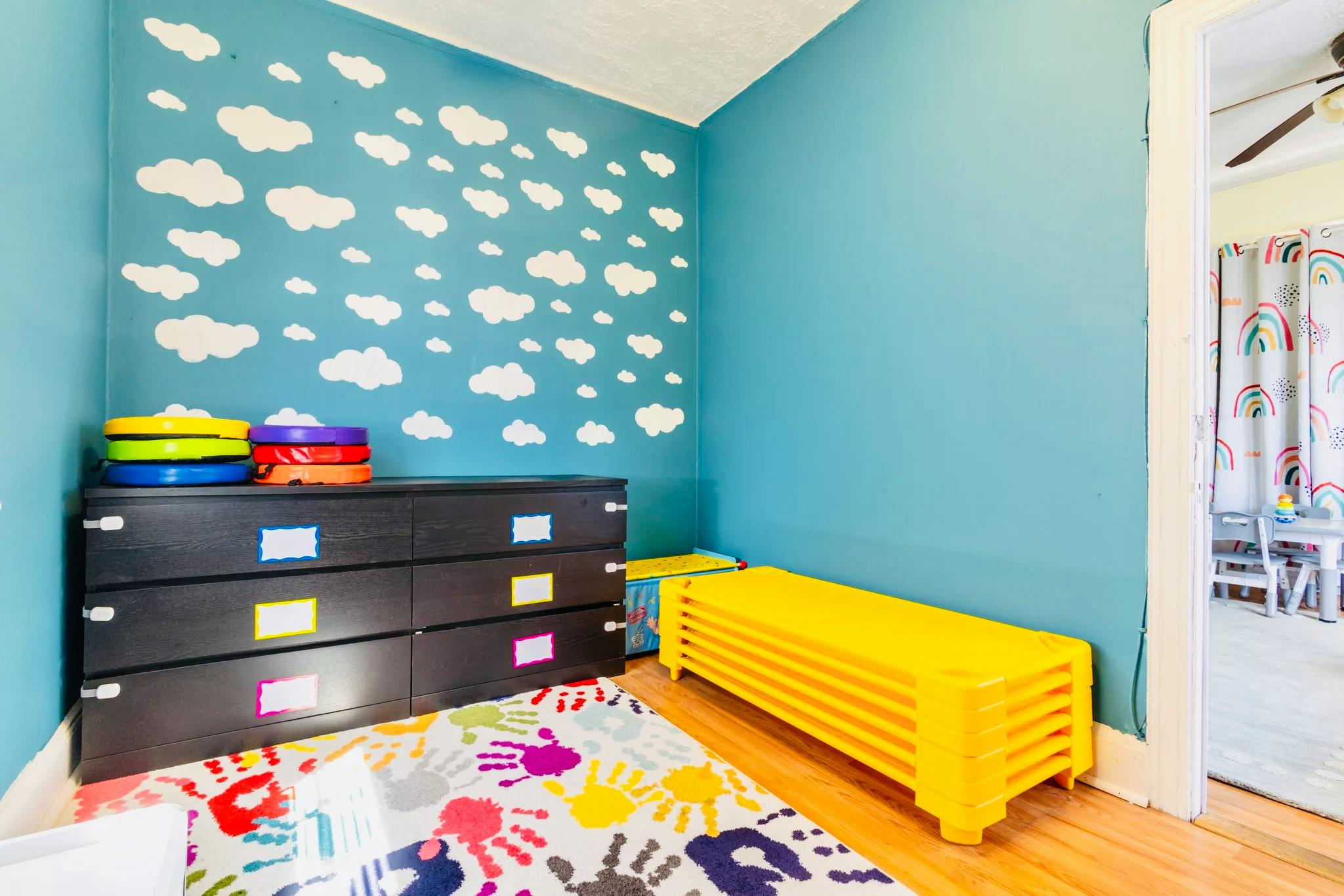 Child's room with blue walls, white cloud decals, a colorful rug, and dark dresser