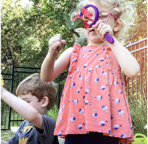 Child holding a flower and a magnifying glass to their eye