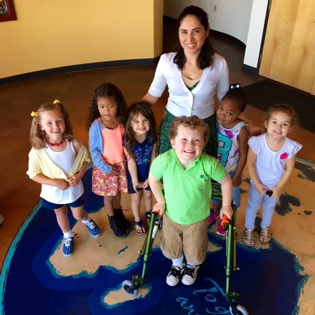 Adult and multiple children standing on a map of the world, one child uses a walker