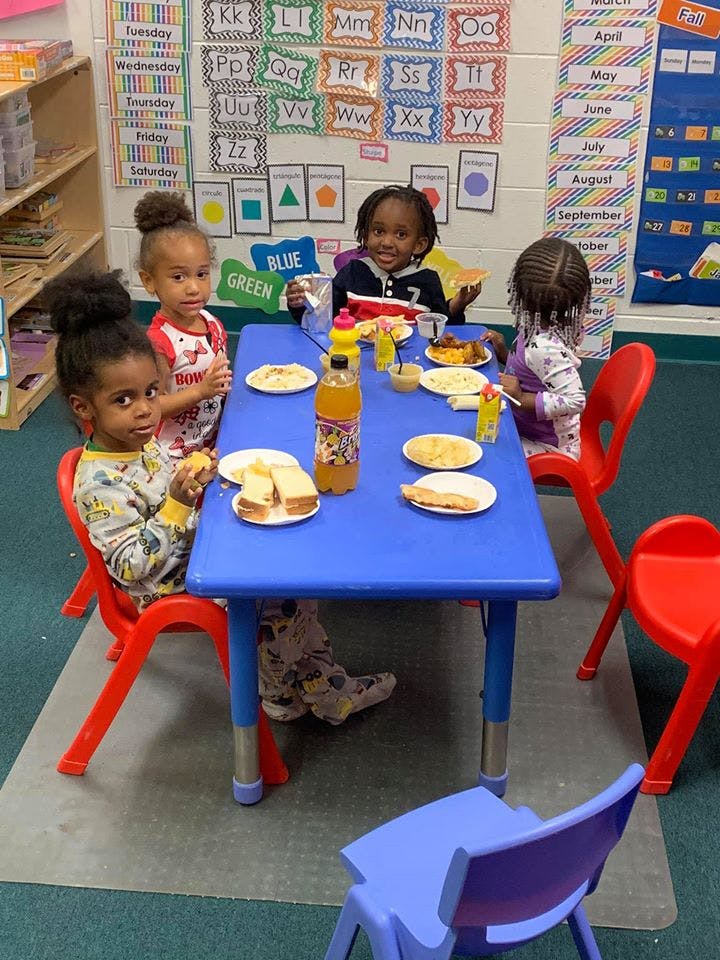 Four children sitting at a blue table with plates of food and drinks