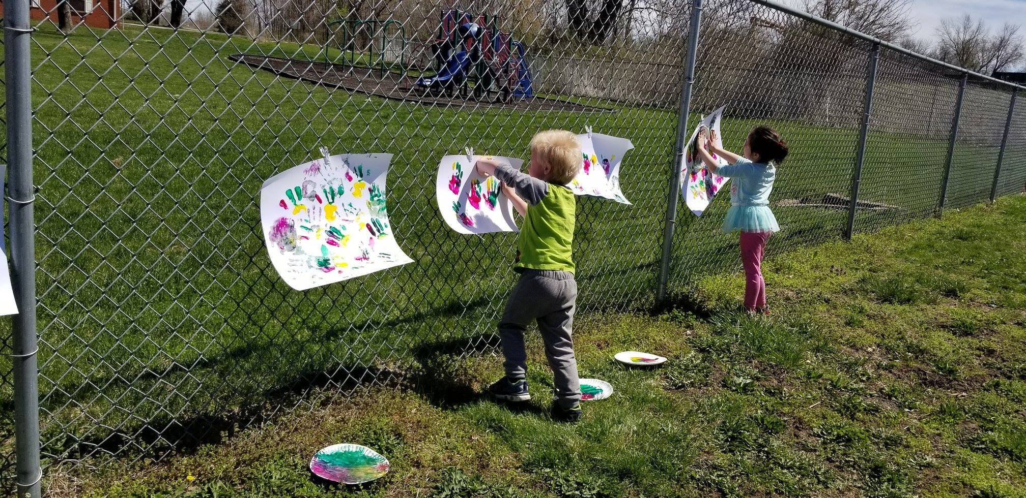 Two children hanging drawings on a chain link fence
