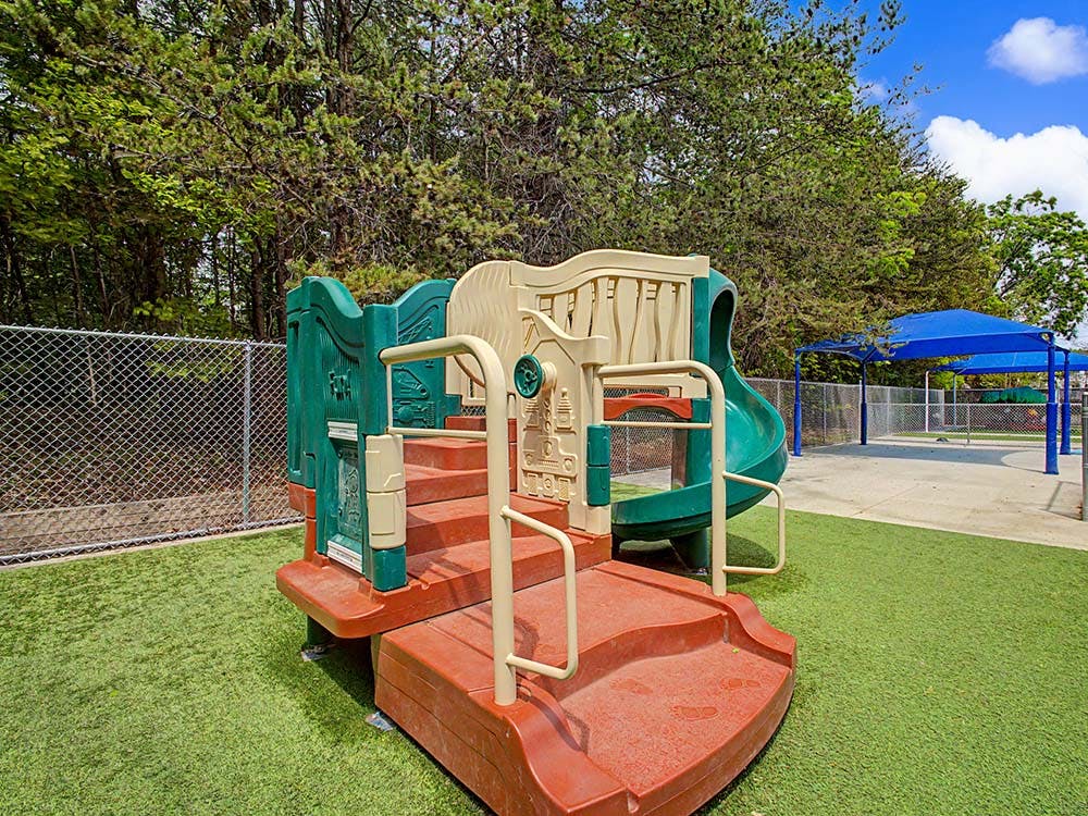 A green and tan playground structure with steps and a slide on artificial turf