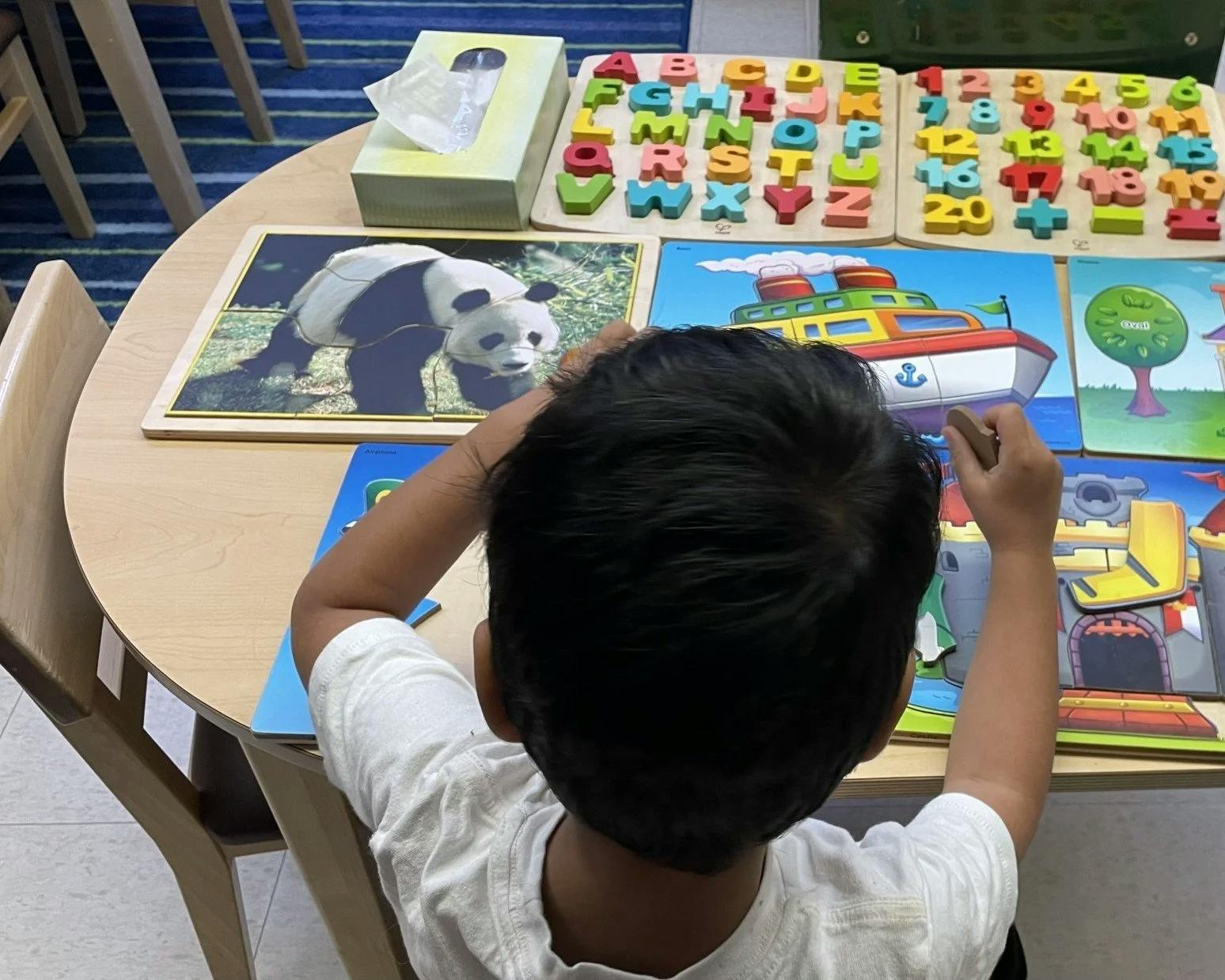Child playing with a puzzle of a boat at a table