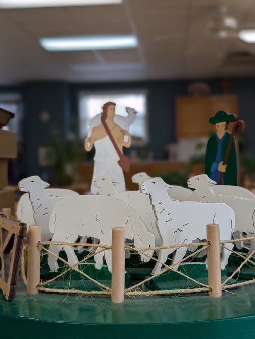 Wooden figures of a person holding a lamb, a person with a staff, and sheep in a pen
