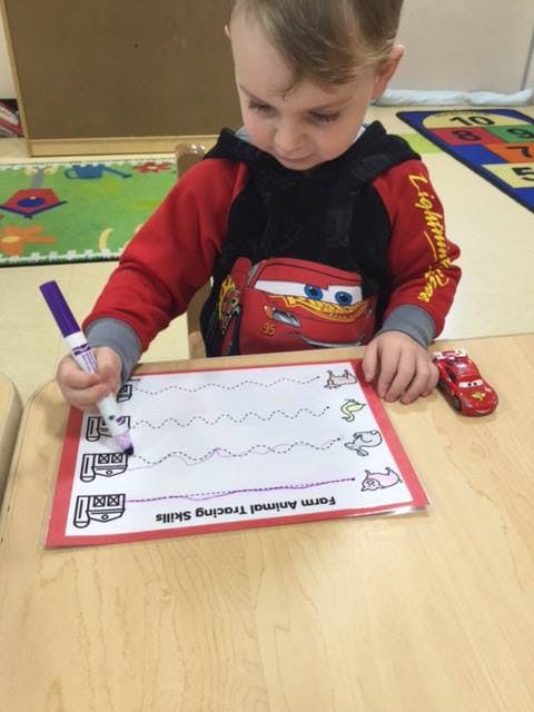 Child tracing lines on a "Farm Animal Tracing Skills" worksheet
