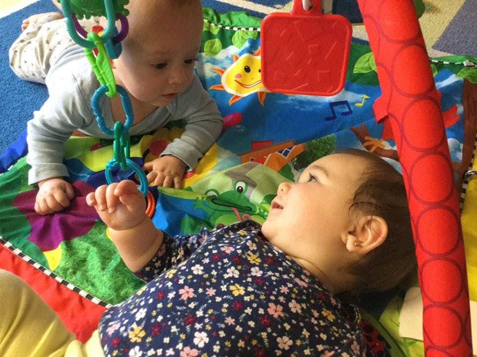 Two children playing on a colorful mat with toys