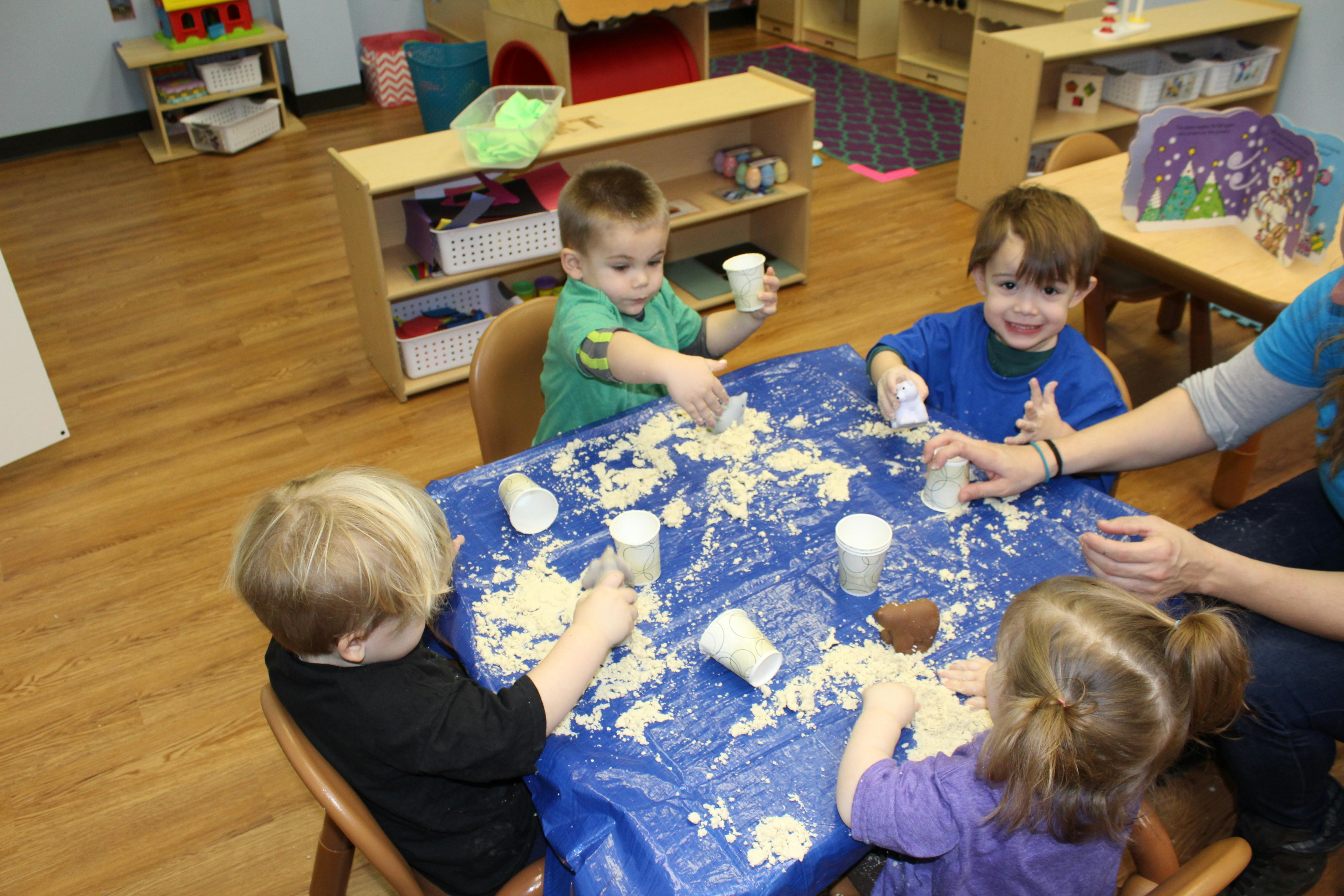 Children playing with sand at a table in a classroom