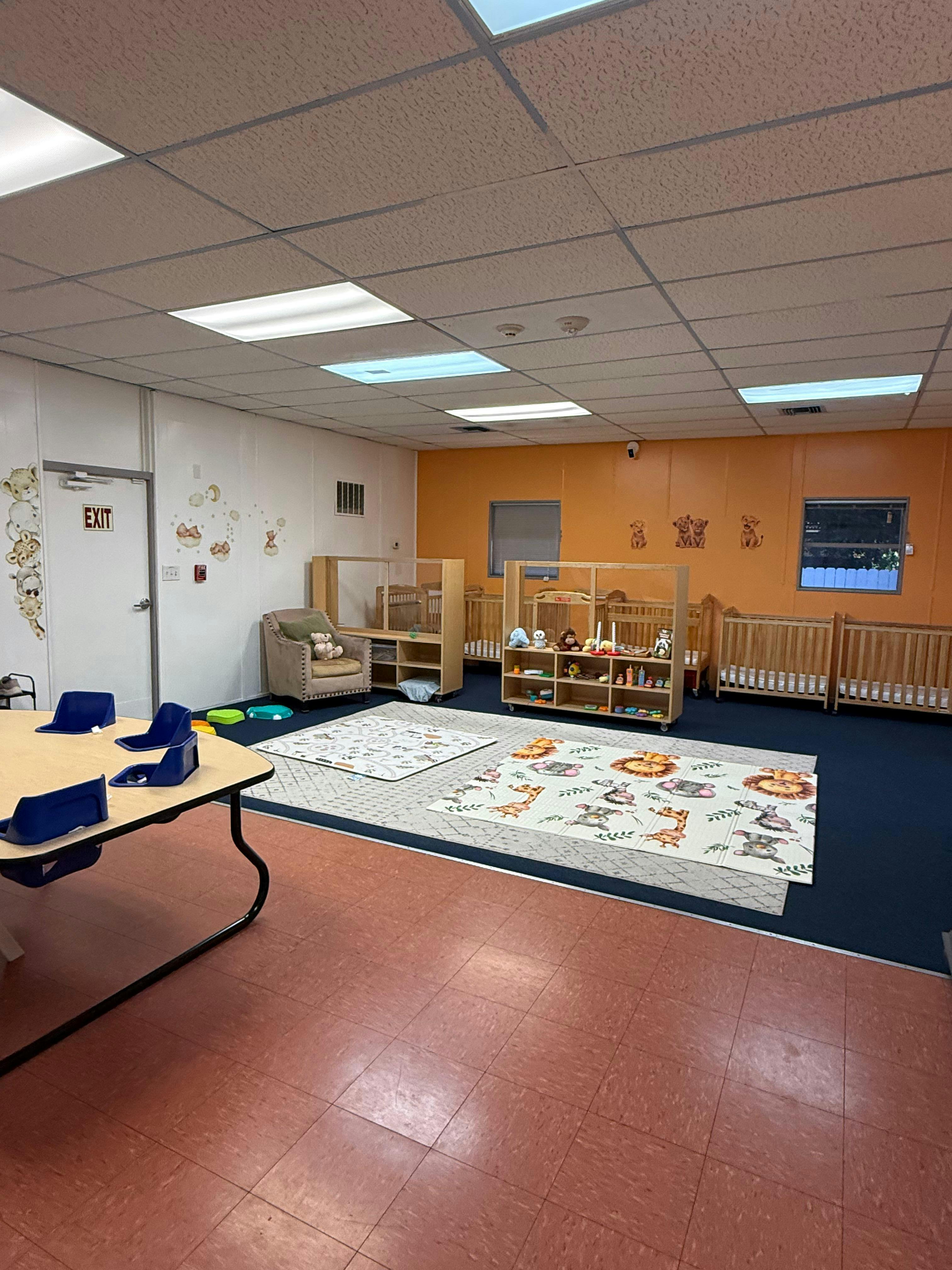 An empty nursery room with cribs, playmats, and a small table with infant seats