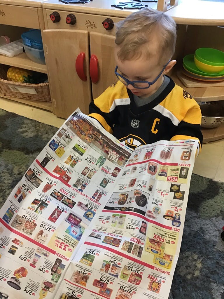 Child wearing glasses and a jersey reading a newspaper