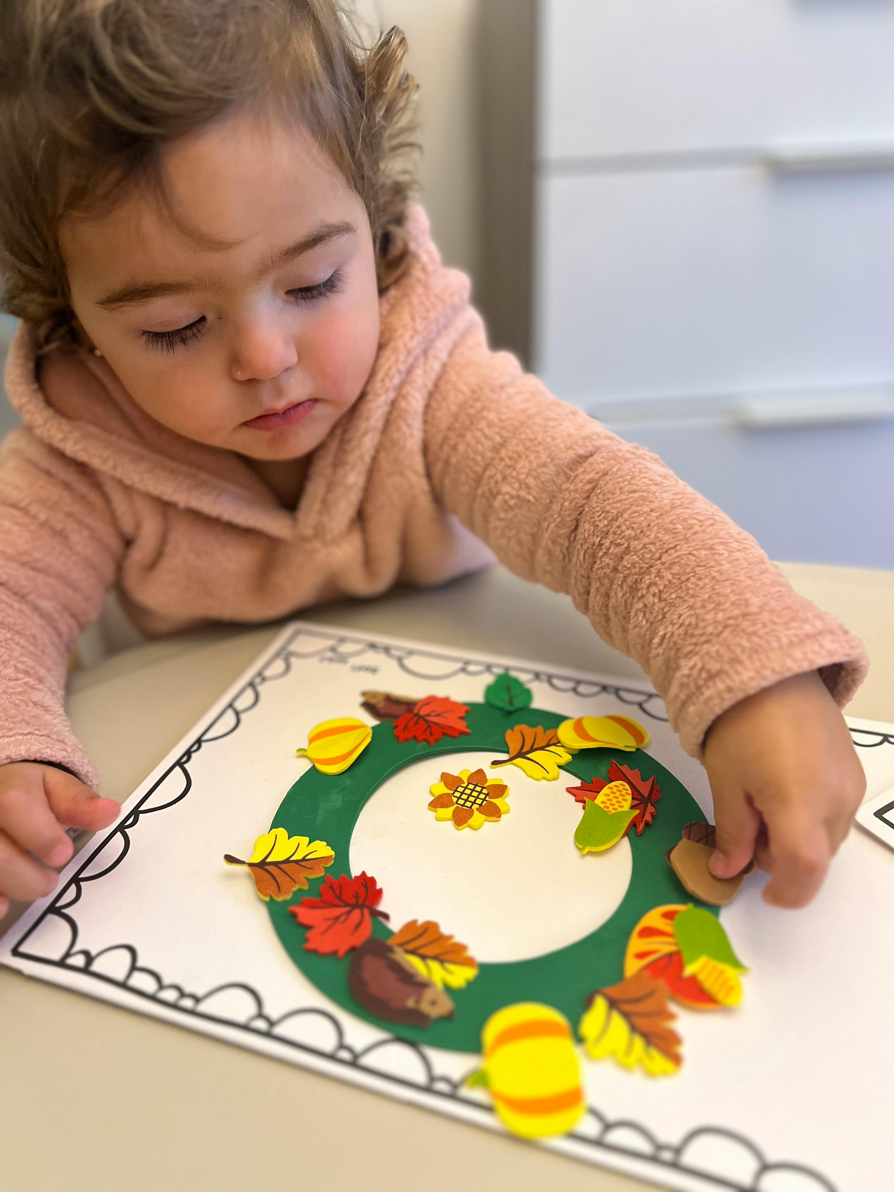 Child creating a fall wreath craft with leaf and acorn cutouts