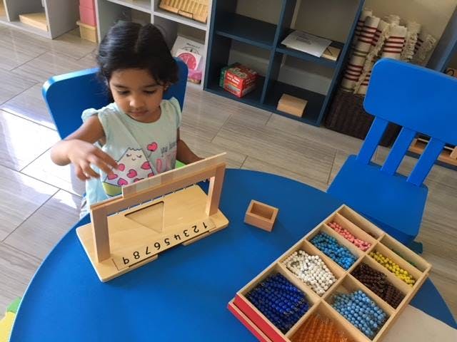 Child playing with a wooden number puzzle at a blue table