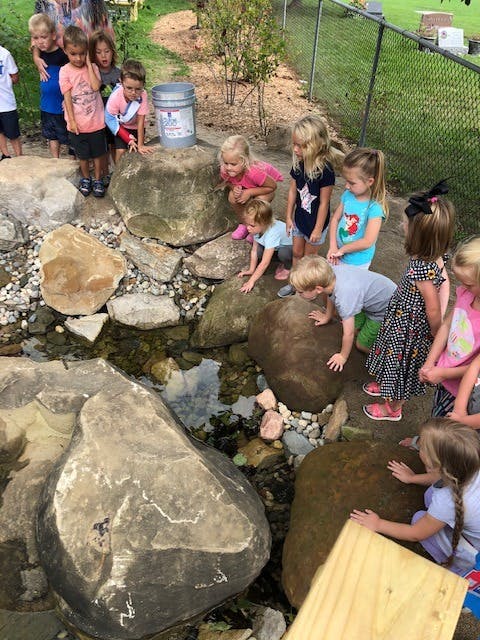 Children gathered around a small stream with rocks