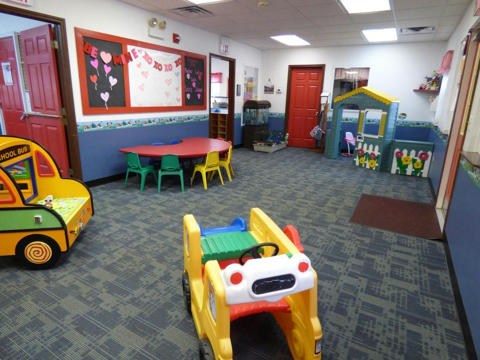 Playroom with small table and chairs, toy bus, and playhouse