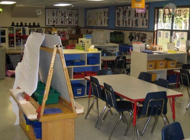 Classroom with child-sized tables and chairs, shelving, and an art easel