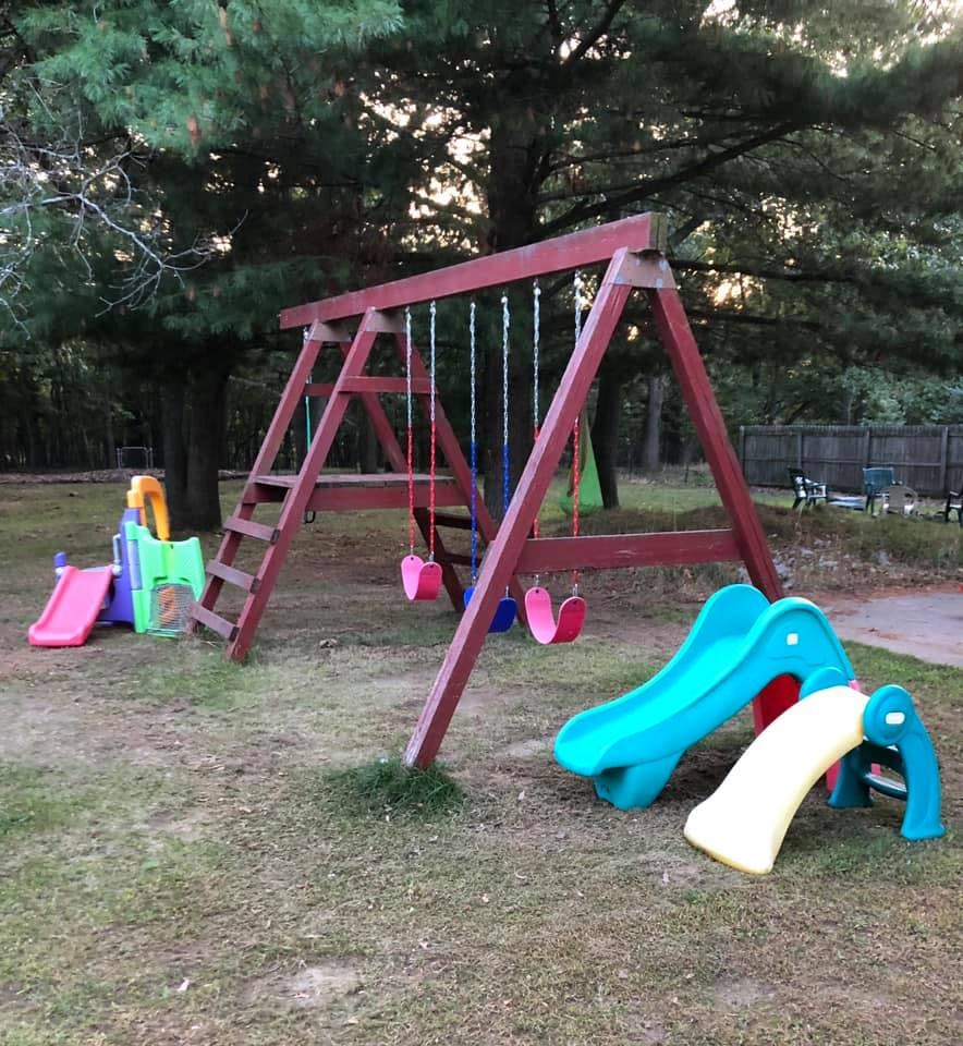 Wooden swing set with multiple swings and plastic slides on grass