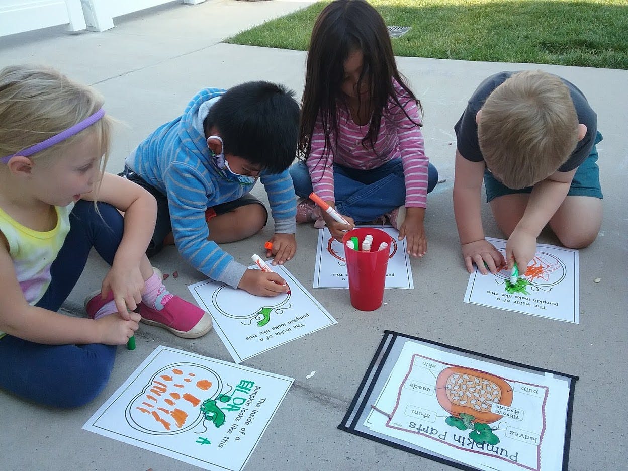 Four children coloring on paper outdoors