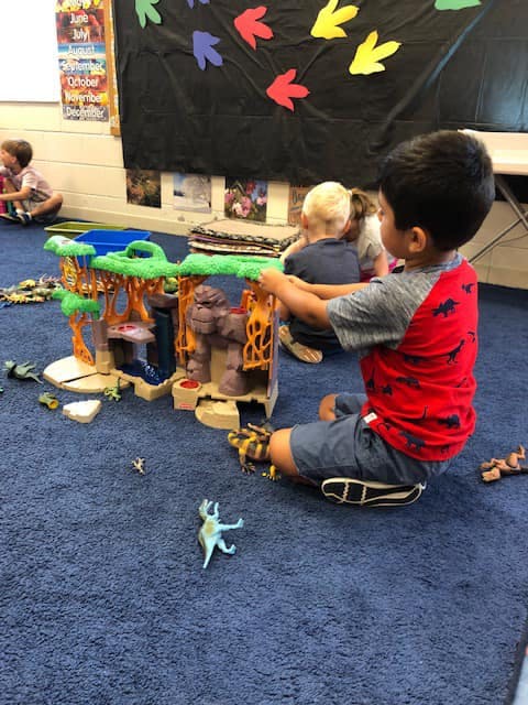 Child playing with a toy playset on a blue carpet in a classroom