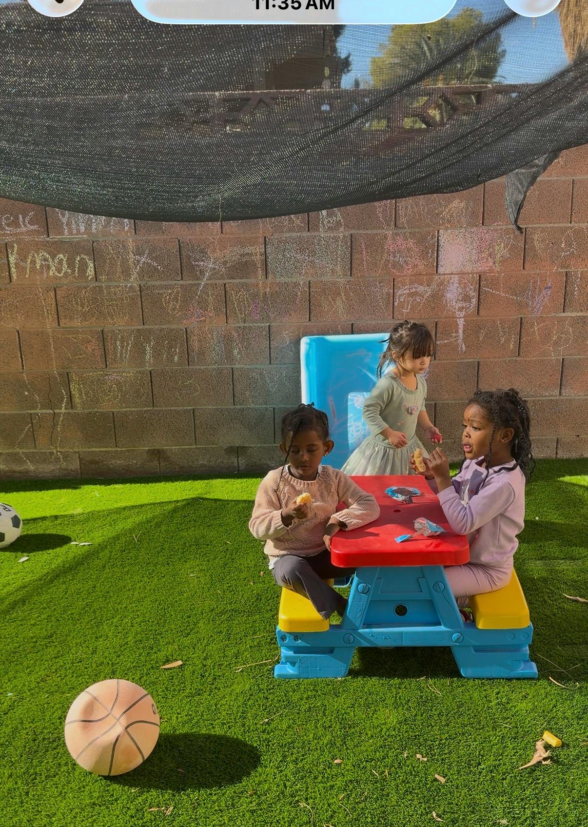 Three children at a colorful picnic table outdoors