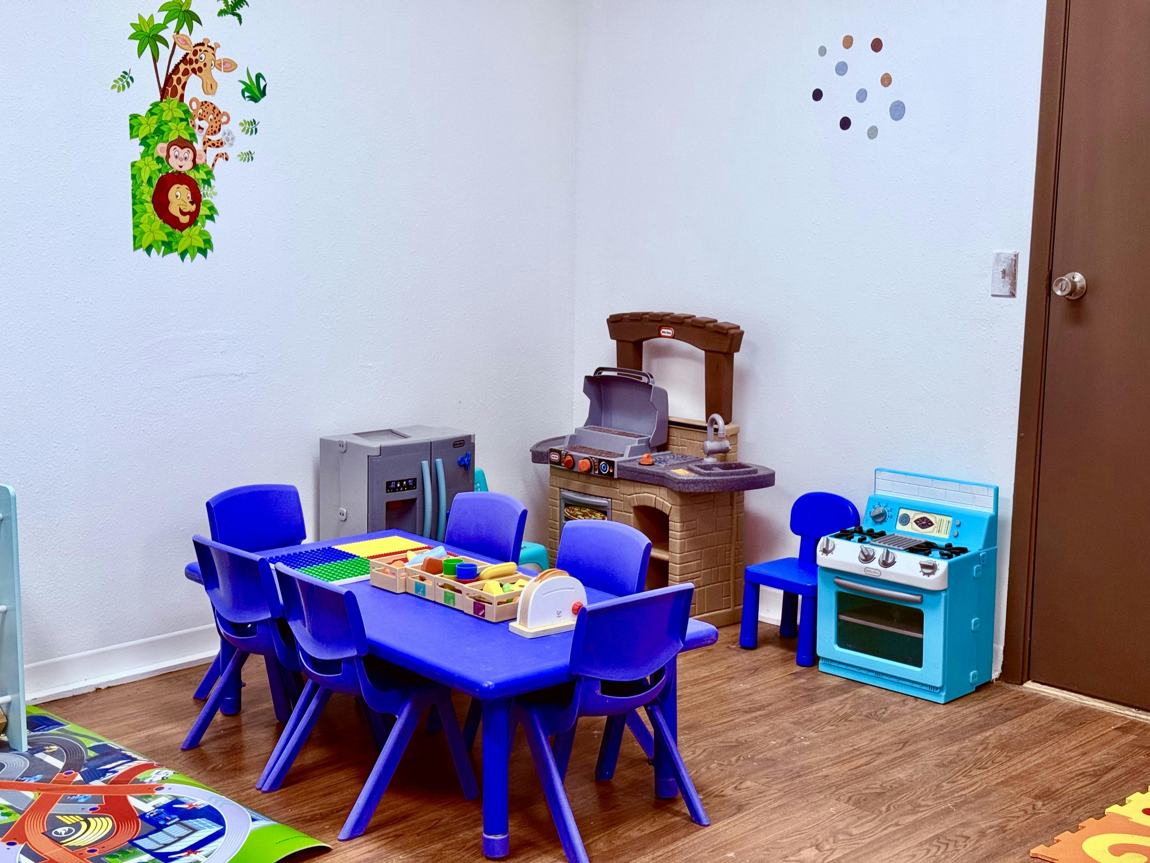 Children's play area with blue table and chairs, toy kitchen, and stove