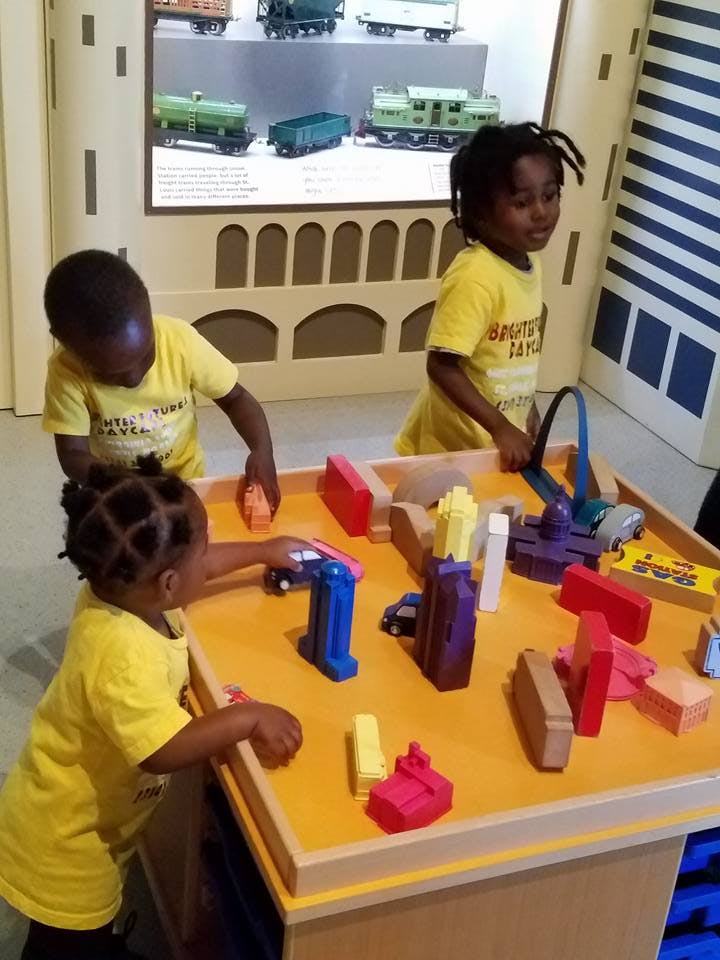 Three children playing with blocks and toy cars on a table