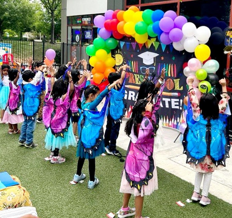 Children in butterfly wings raising their arms under a balloon arch