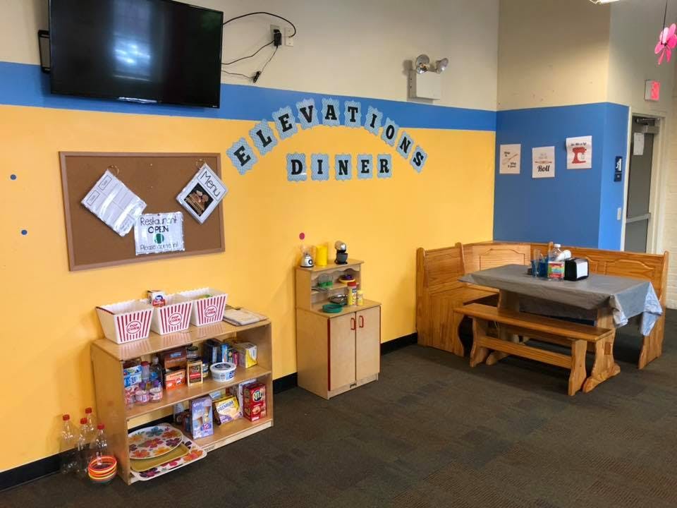 Playroom with yellow and blue walls, a wooden booth, and a shelf with toys
