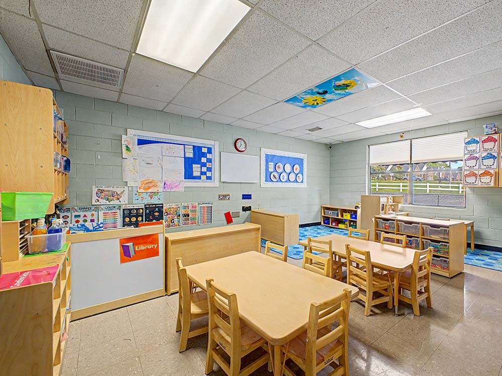 Classroom with small wooden tables and chairs, and a 'Library' sign on a counter