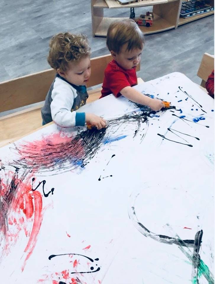 Two children painting on a large sheet of paper