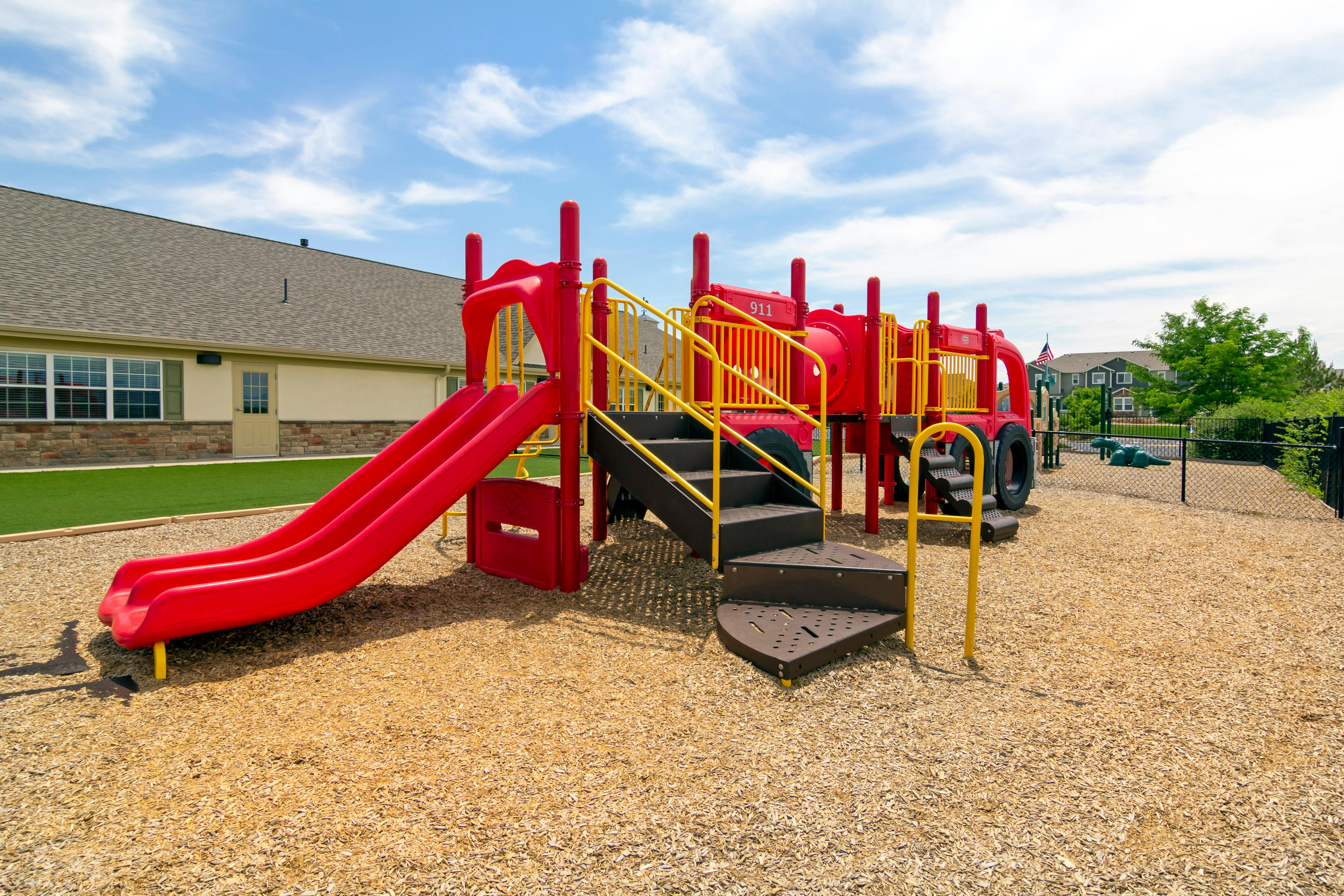 Red and yellow playground with slides and steps on wood chips