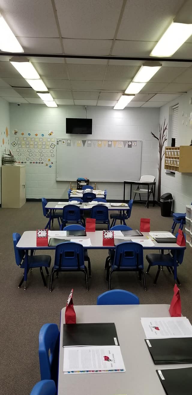 Classroom with small tables and blue chairs, whiteboard, and wall decorations