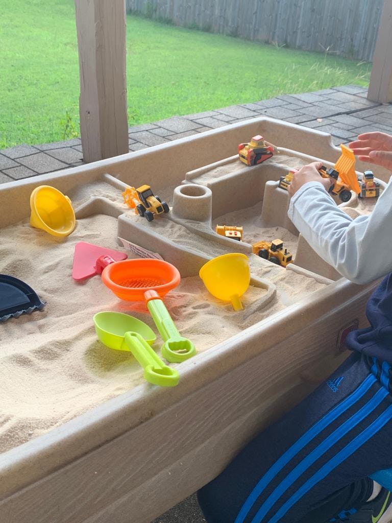 Child playing in a sandbox with toy construction vehicles and sand tools