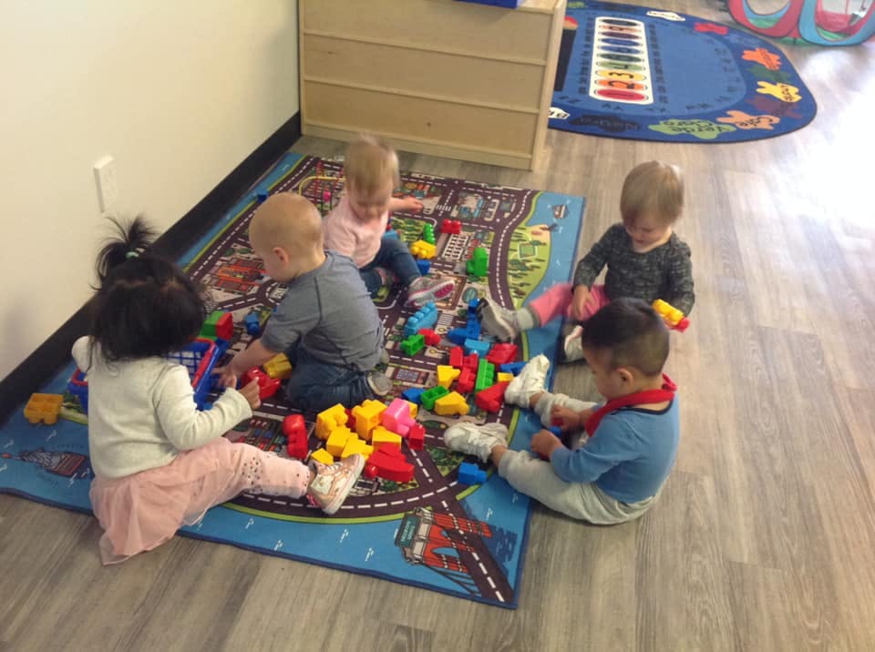 Multiple children playing with colorful building blocks on a rug