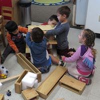 Four children playing with wooden blocks on the floor