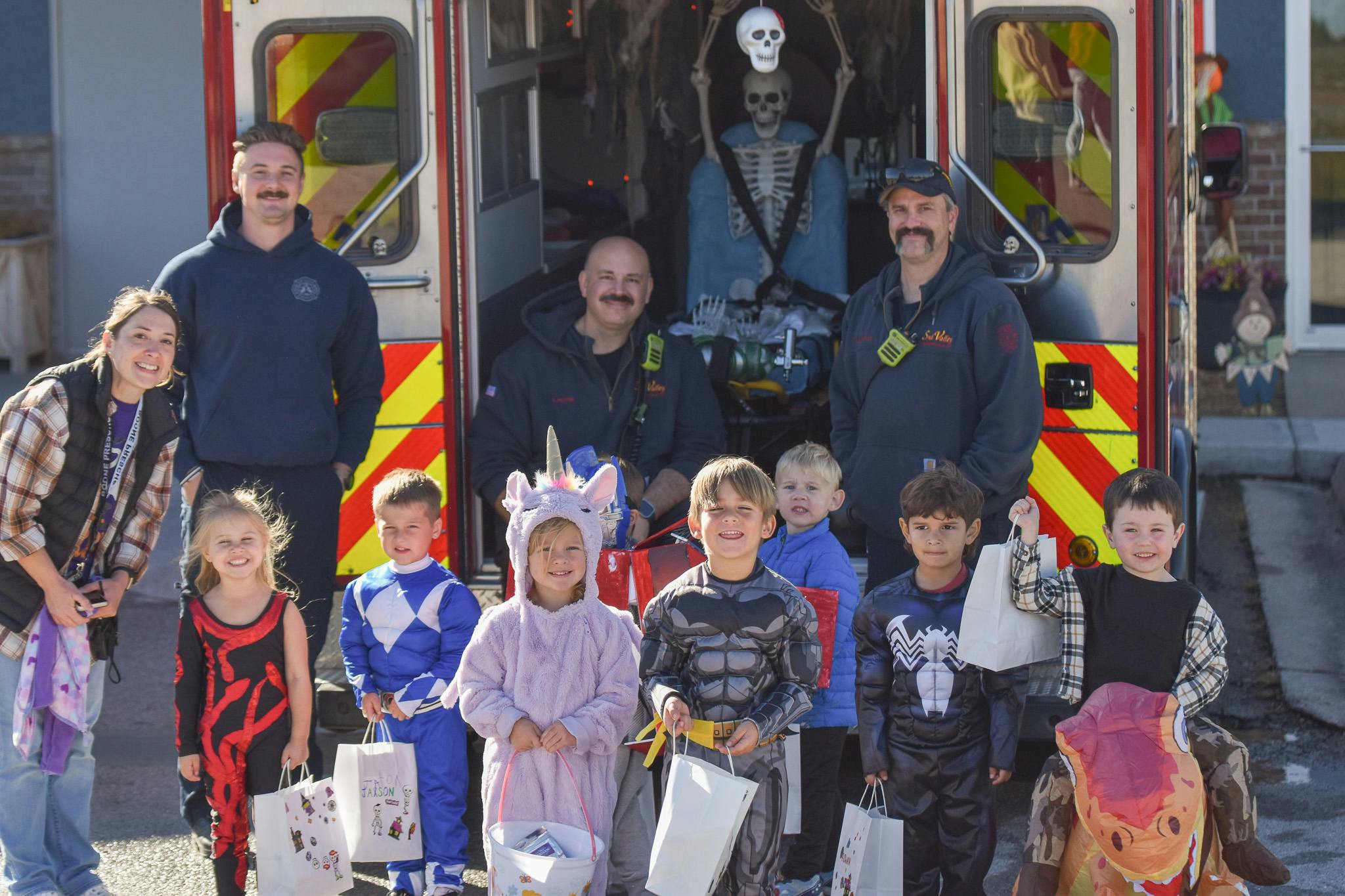 People in uniform and children in Halloween costumes holding trick-or-treat bags