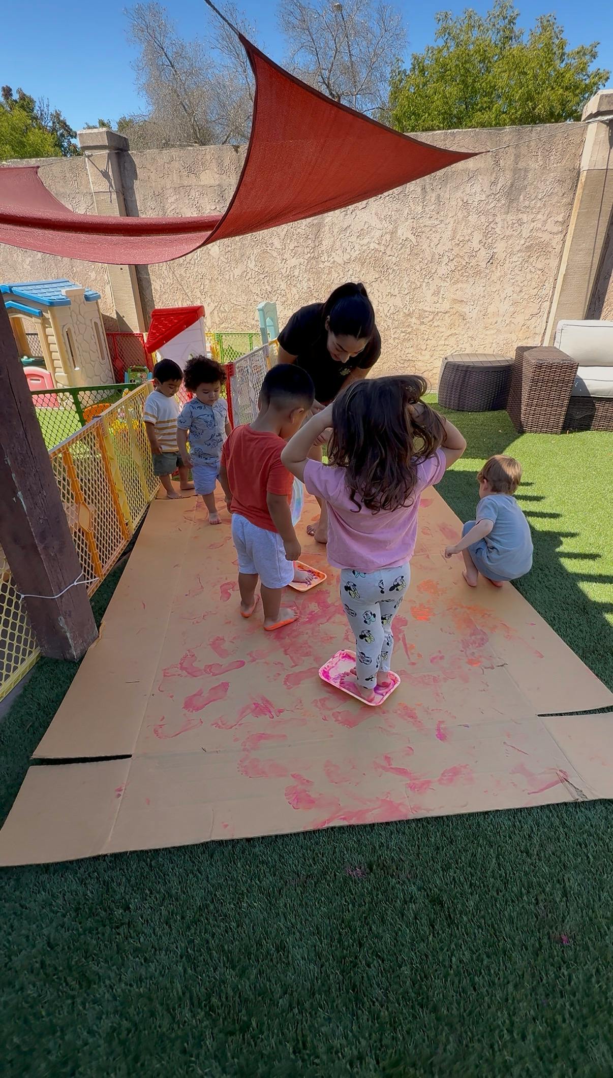 Adult and several children doing foot painting on cardboard outdoors