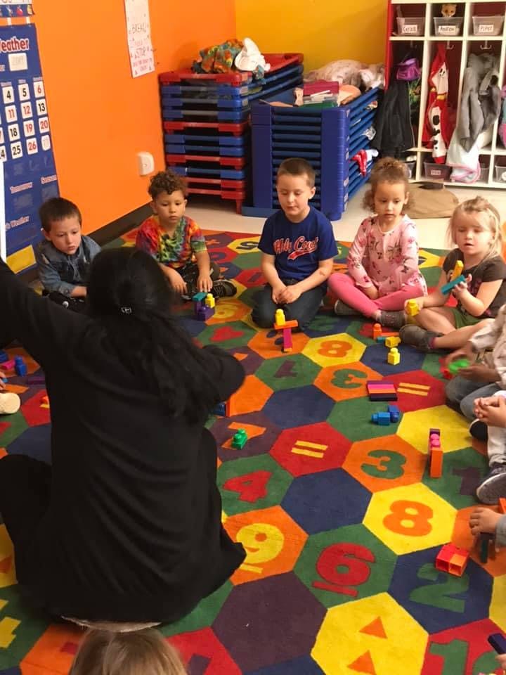 Adult and children sitting on a colorful rug with blocks