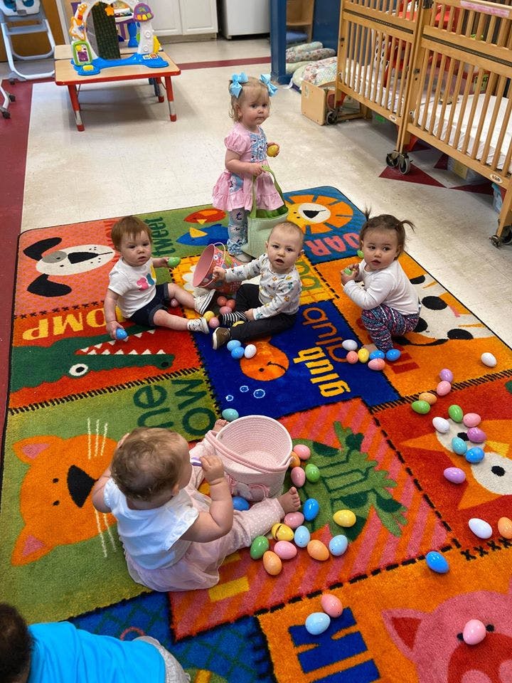 Multiple children playing with plastic eggs and buckets on a colorful rug