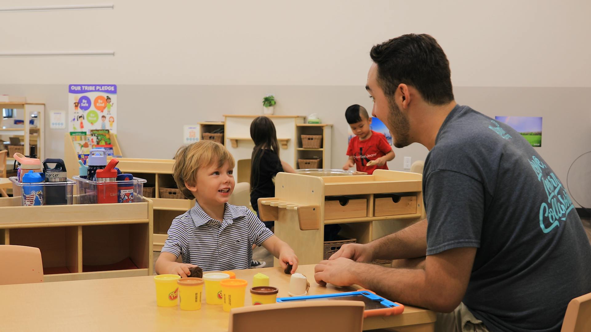 Adult and child interacting at a table in a classroom