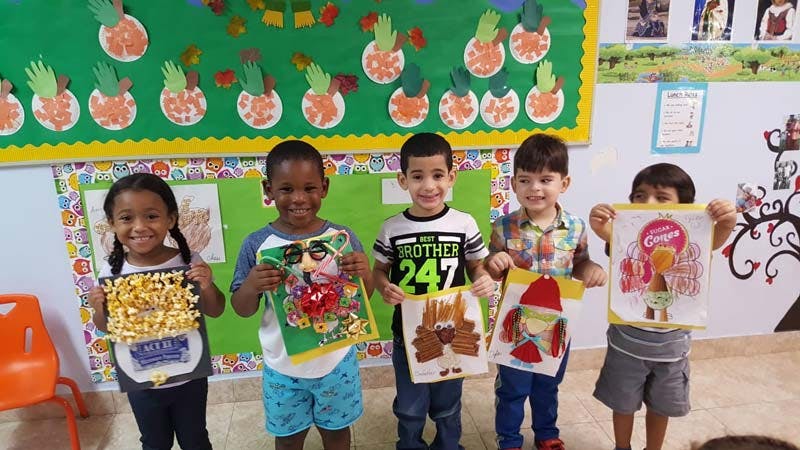 Five children holding up their artwork in a classroom