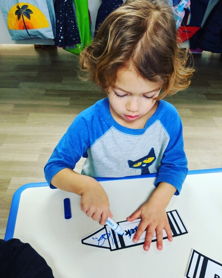 Child coloring a paper crayon cutout with a marker