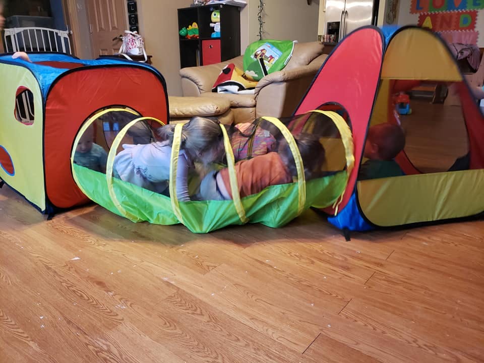 Child crawling through a play tunnel connected to a play tent