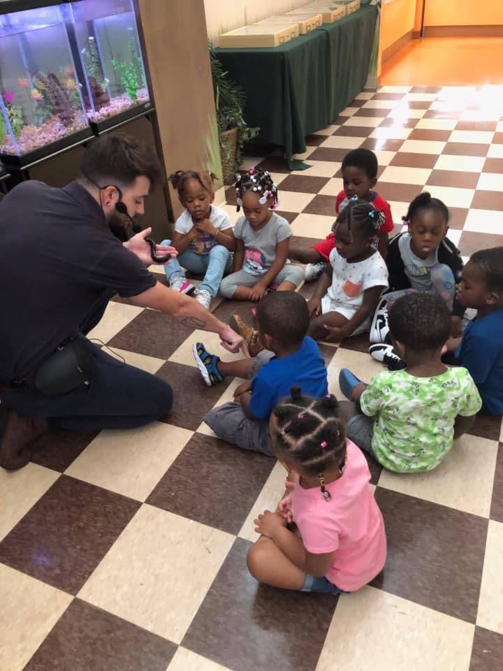 Adult kneeling and talking to a group of children sitting on the floor