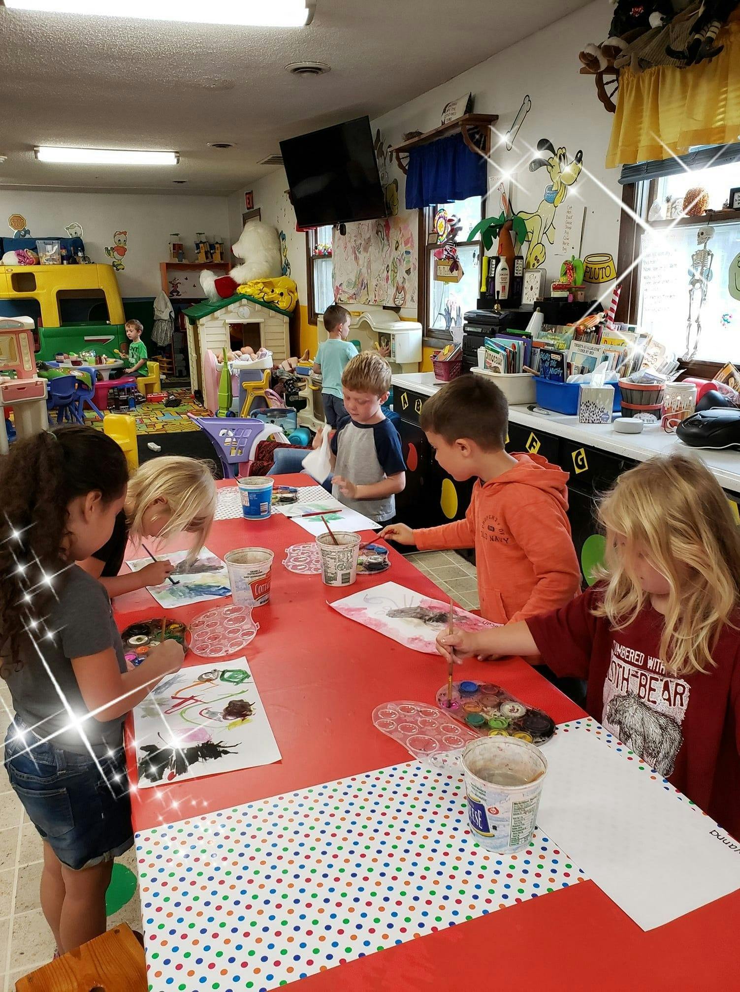Children painting at a long red table in a classroom