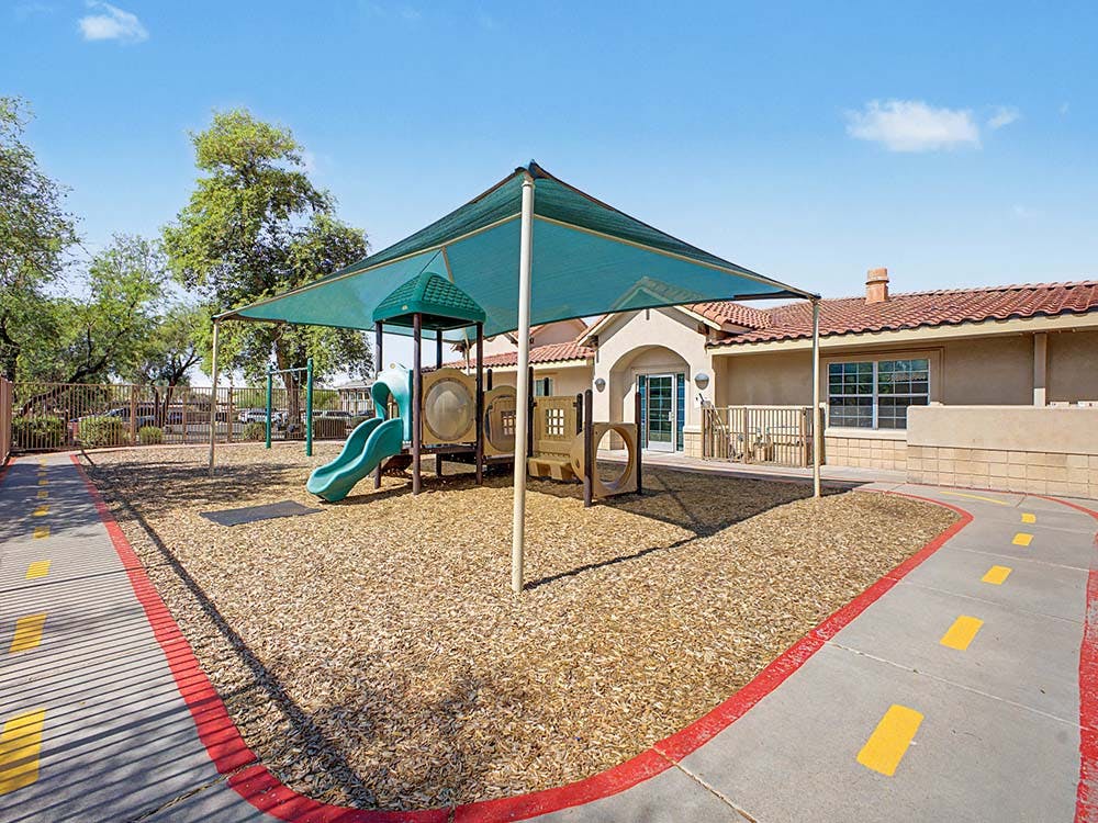Playground with wood chips and a green slide under a shade cover