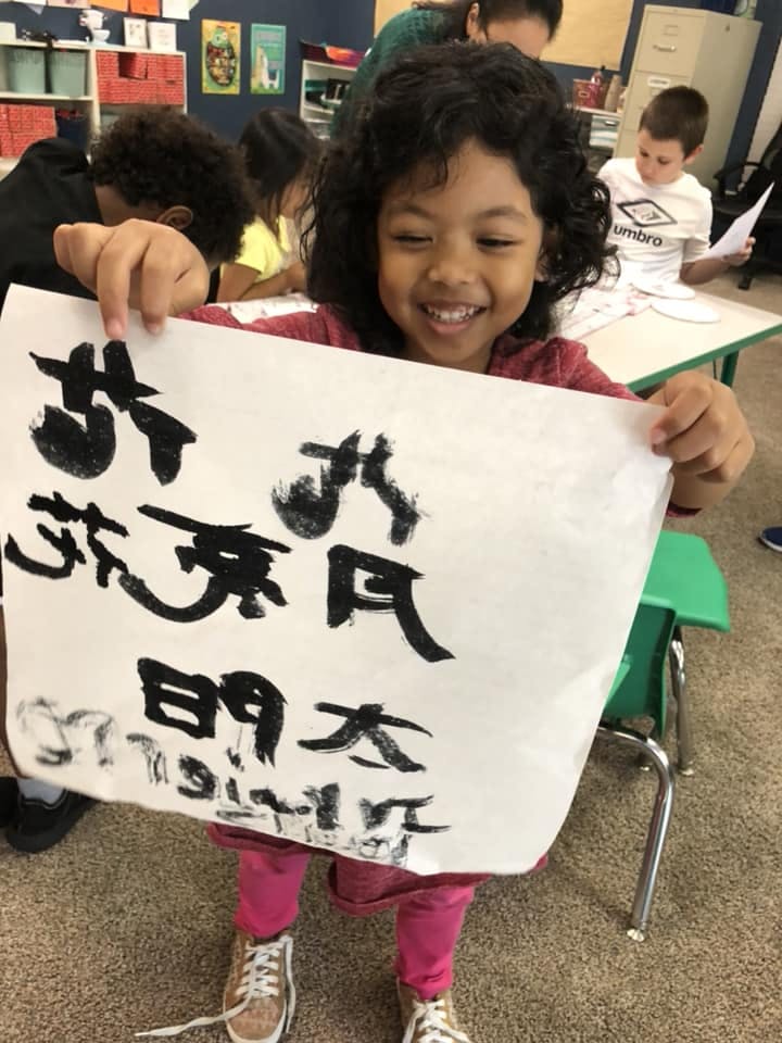 Child holding up a paper with black brushstroke characters