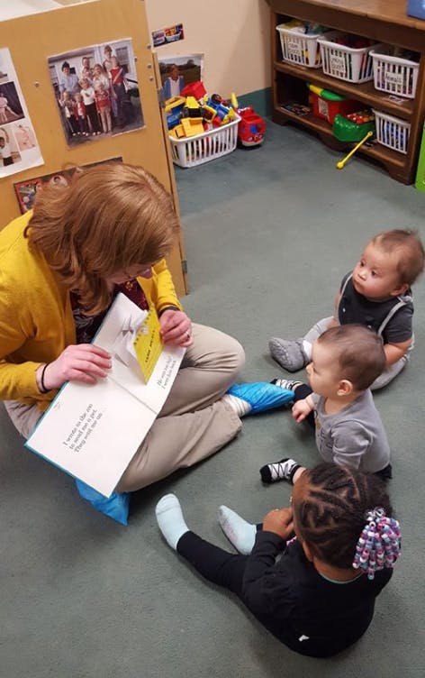 Person reading a book to three children on the floor