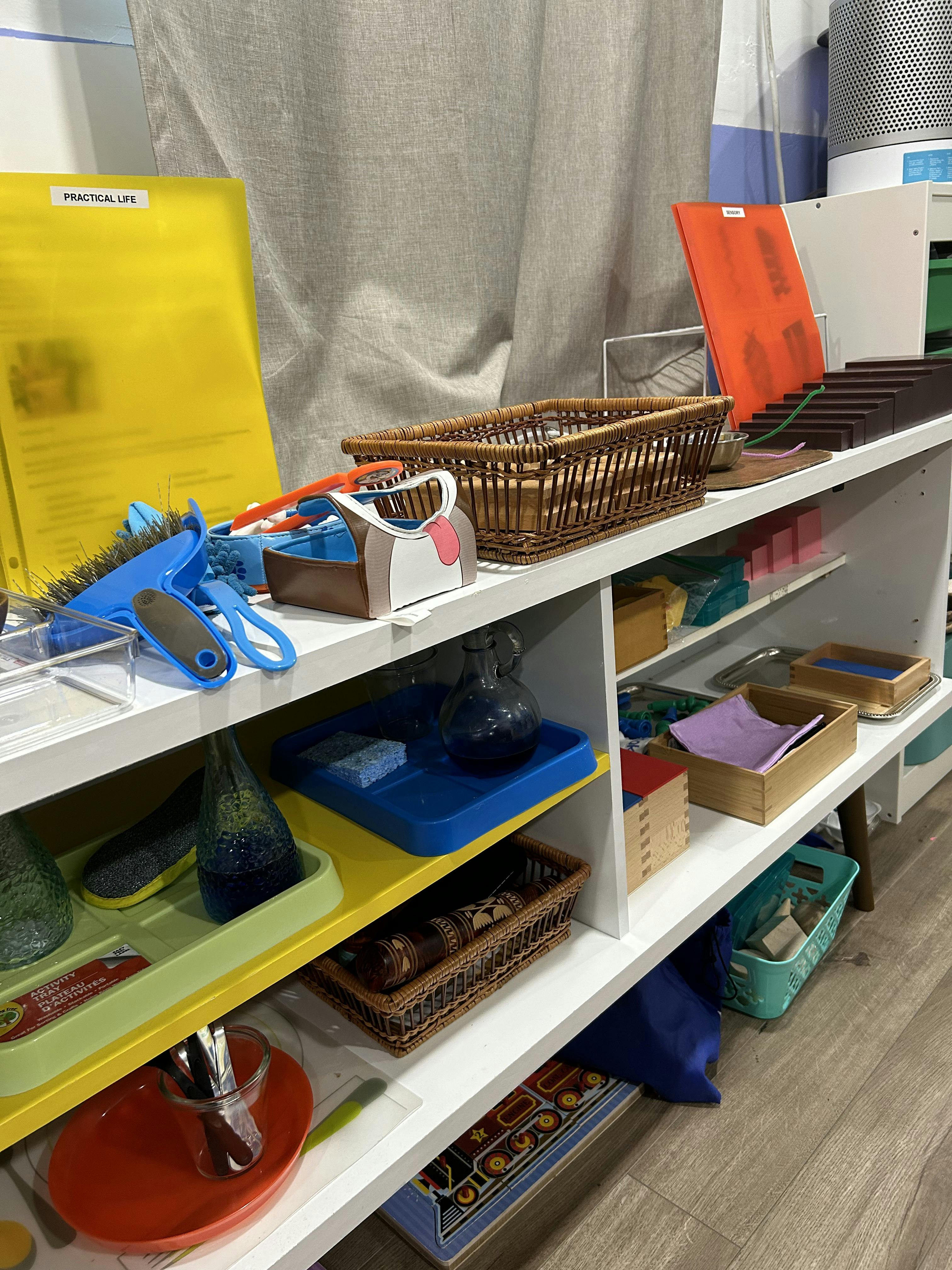 Shelves with various items including baskets, trays, and a yellow folder labeled "PRACTICAL LIFE"